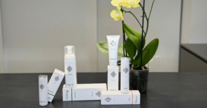 Linea di cosmetici “Interactive” di Rejuve, esposta su una superficie nera con sfondo neutro e un’orchidea gialla in vaso accanto ai prodotti
