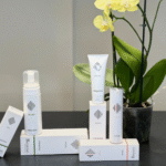 Rejuve cliniceutical products arranged on a black surface next to a potted yellow orchid. The white packaging displays the logo and names of the "Interactive", "Restore", and "Cure" product lines.
