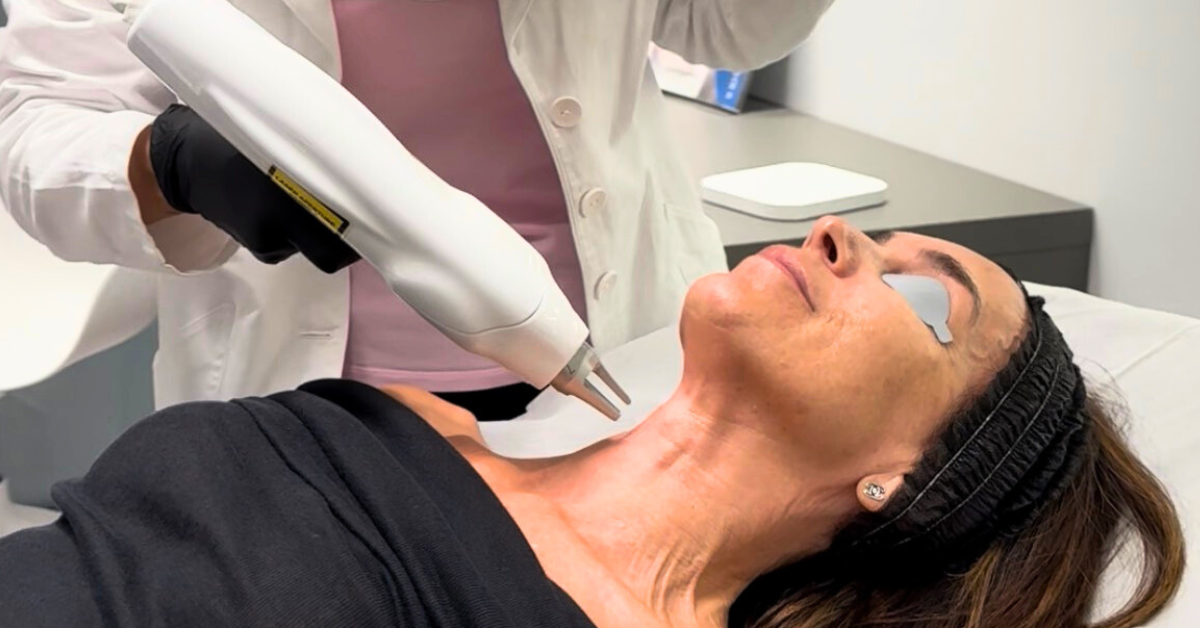 Donna sdraiata durante un trattamento estetico con dispositivo laser sul collo, eseguito da un’operatrice medica.